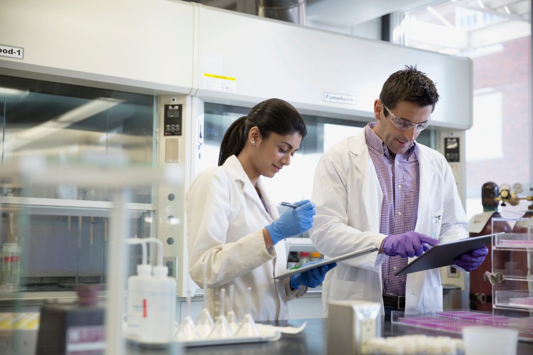Two lab scientists in protective gloves reviewing results on tablets