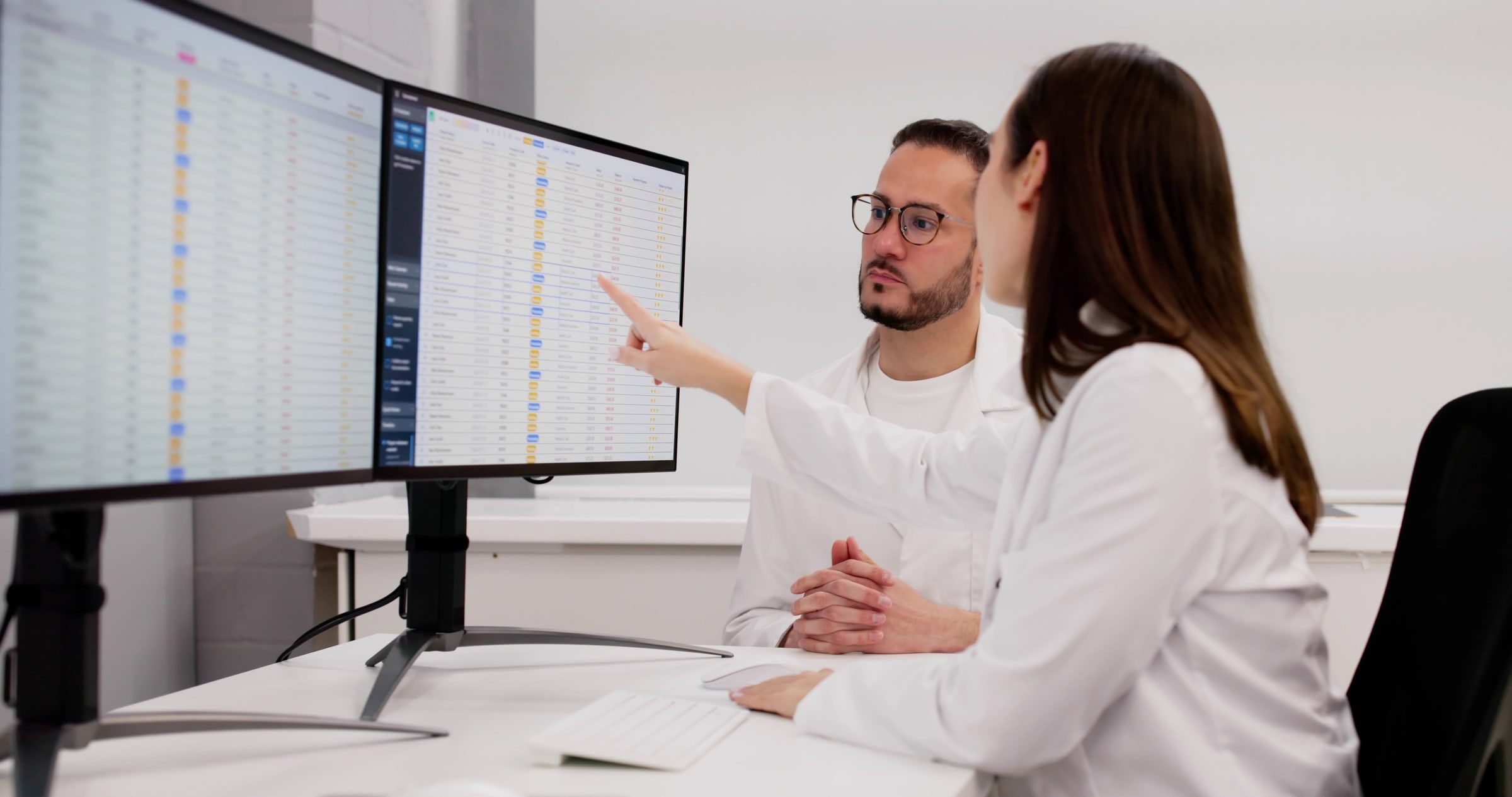 Two lab staff reviewing billing data on a monitor