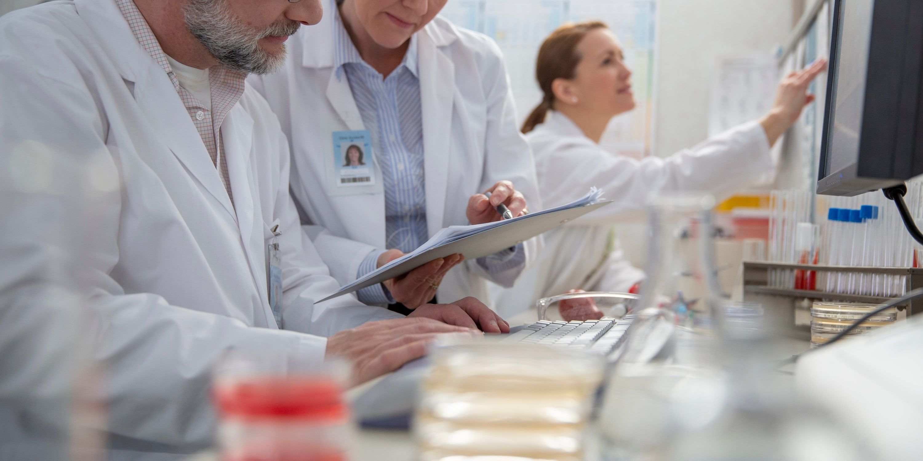 Lab technicians reviewing a test requisition on a clipboard, with DocKnow highlighting the collection date, specimen ID, policy number, and patient name fields it extracts