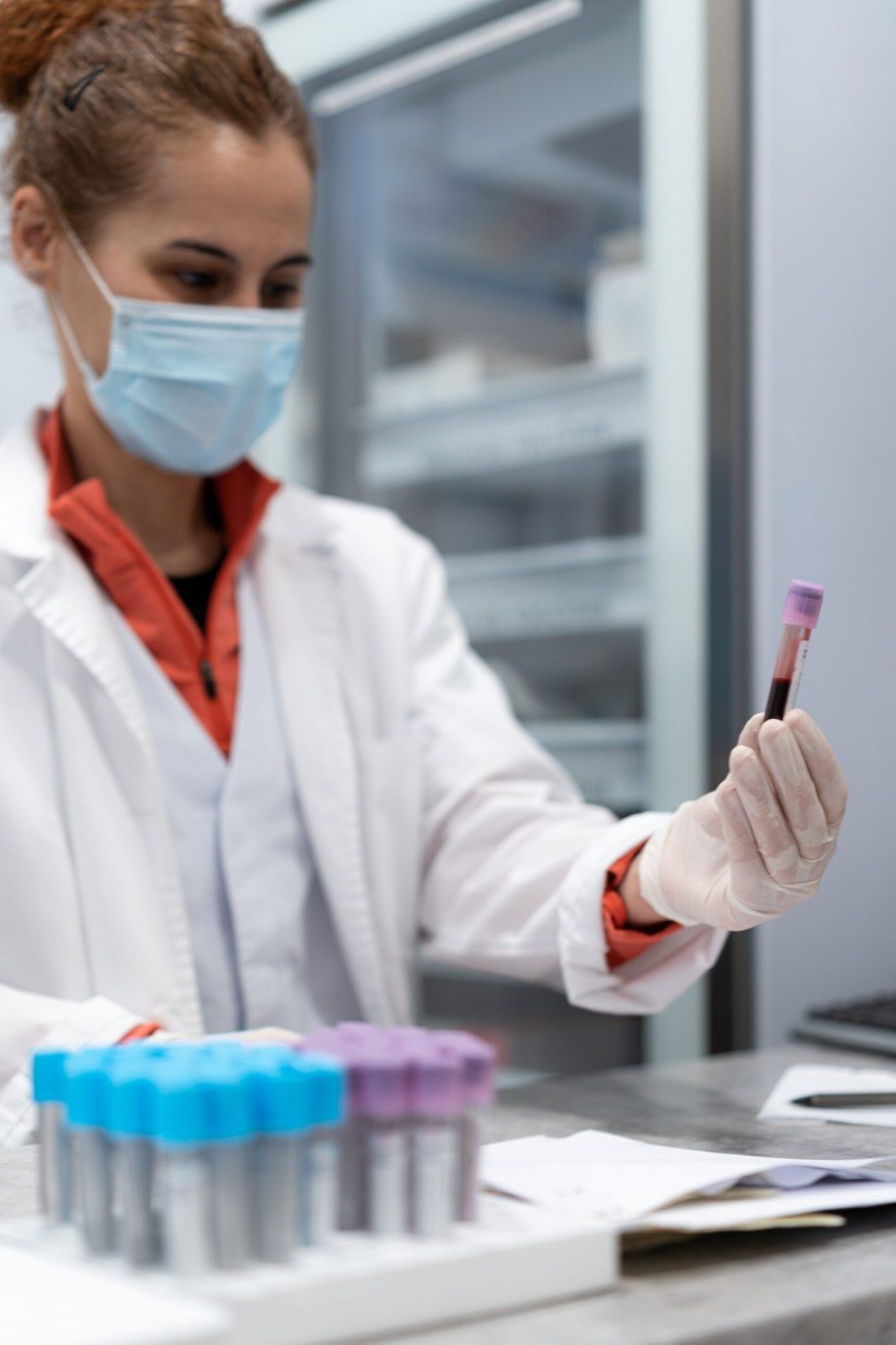 Scientist in a mask holding a blood sample tube at a lab bench